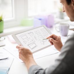 A product designer in a bright workspace reviewing interface sketches on a tablet